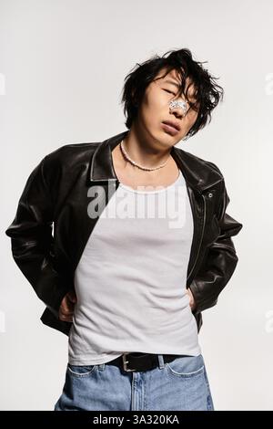 Asiatischer Mann in Lederjacke und Gips an der Nase posiert selbstbewusst und zeigt einen modernen Stil. Stockfoto