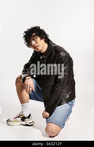 Junger asiatischer Mann mit Gips auf der Nase in stilvoller Kleidung kniend für ein Studio-Modeschuss. Stockfoto