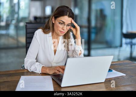 Müde, besorgte ältere Geschäftsfrau mit Brille und Kopfschmerzen bei der Arbeit. Stockfoto