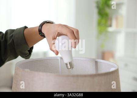 Mann wechselt Glühbirne in Lampe zu Hause, Nahaufnahme Stockfoto