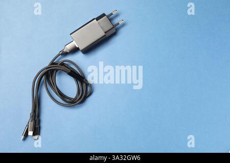 USB-Netzteil mit dreifachem Ladekabel auf hellblauem Hintergrund, Draufsicht. Leerzeichen für Text Stockfoto