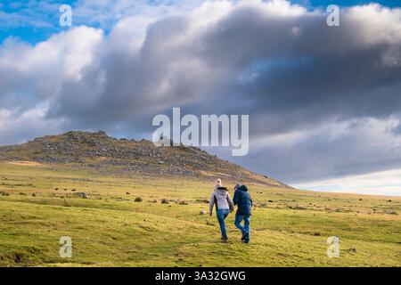 Zwei Personen gehen auf den imposanten Granitgrat Roughtor Rough Tor auf dem wilden windgepeitschten Bodmin Moor in Cornwall in Großbritannien. Stockfoto