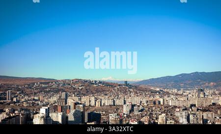 Ein Panoramablick auf eine geschäftige Stadt, umgeben von Hügeln und Bergen unter einem klaren blauen Himmel. Die urbane Landschaft bietet eine Mischung aus Moderne und Tradition Stockfoto