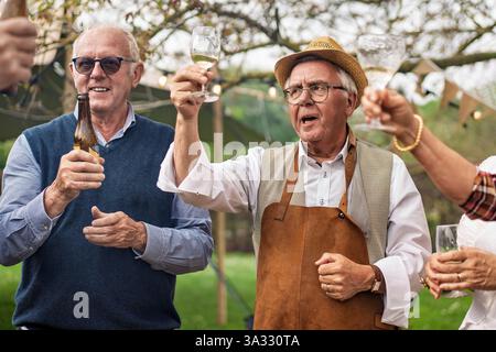 Gruppe von Seniorenfreunden, die bei einer Gartenparty im Freien Wein und Bier trinken, gesellige Momente genießen und gemeinsam feiern. Fröhliche ältere Menschen Stockfoto