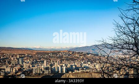 Panoramablick auf Tiflis, Georgien, mit dem schneebedeckten Kaukasus im Hintergrund an einem klaren Wintertag. Die Skyline der Stadt ist ein schöner Kontrast Stockfoto