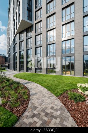 Pfad in einem Garten in der Nähe eines modernen Bürogebäudes. Grüne Gegend im Stadtzentrum - kurviger Fußweg zwischen Büschen. Stockfoto