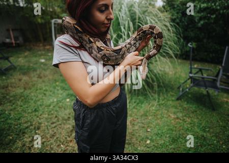 Mädchen, das sanft eine große Schlange in einem Garten umgeht Stockfoto