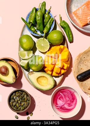Draufsicht auf verschiedene frische Zutaten für die Taco-Zubereitung auf einem leuchtend rosa Hintergrund. Das Bild zeigt grüne Paprika, geschnittene Limetten, Avoc Stockfoto