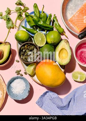 Draufsicht auf frische Zutaten für Tacos auf einem leuchtend rosa Hintergrund. Einschließlich Lachs, Avocados, Limetten, Mango, grüne Chilischoten, Koriander, Kürbis Stockfoto