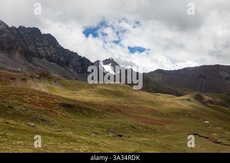 Dieses lebendige Bild fängt die atemberaubende natürliche Schönheit der peruanischen Andenberge mit üppigen grünen Feldern und zerklüfteten Gipfeln ein, die teilweise mit bedeckt sind Stockfoto