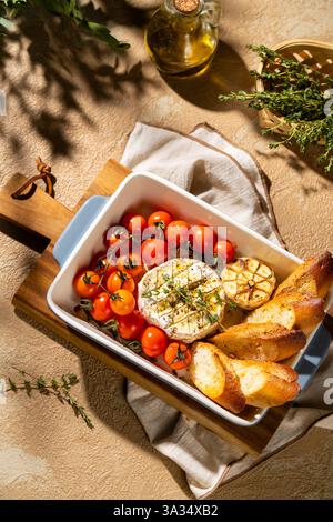 Genießen Sie den Anblick von gebackenem Camembert mit Kirschtomaten, Knoblauch und frischen Kräutern. Abgerundet wird das Gericht mit gerösteten Baguette-Scheiben, die ein Delig bieten Stockfoto