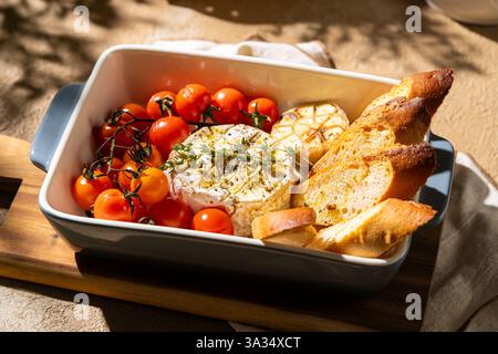 Ein köstlicher gebackener Camembert-Käse, serviert mit gerösteten Kirschtomaten und knusprigen Brotscheiben. Perfekt garniert mit Kräutern bietet dieses Gericht eine Stockfoto