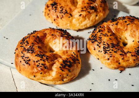 Ein Nahbild von drei goldbraunen Bagels, bestreut mit schwarzen Sesamsamen, auf einer mit Pergament gefüllten Oberfläche. Perfekt für Bäckerei, Frühstück, o Stockfoto