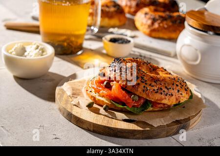Ein frisch gebackener Sesambagel mit Räucherlachs, Kapern und Frischkäse auf einem rustikalen Holzbrett. Ein perfekter Snack zum Frühstück oder Brunc Stockfoto