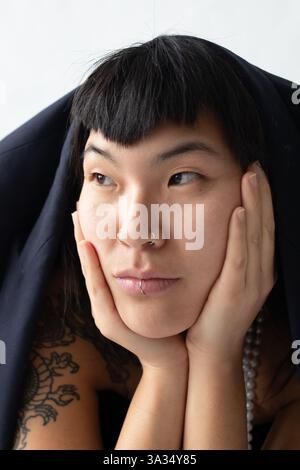 Ein Nahporträt einer jungen asiatischen Frau mit dunklen Haaren, Pony und Gesichtspiercings. Stockfoto
