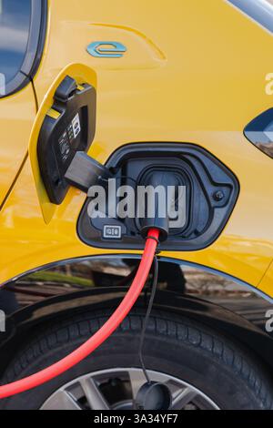 Nahaufnahme eines Elektroautos, das mit einem leuchtend roten Kabel an einer Station aufgeladen wird. Der komplizierte Ladeanschluss des gelben Fahrzeugs ist sichtbar und unterstreicht die Moderne Stockfoto