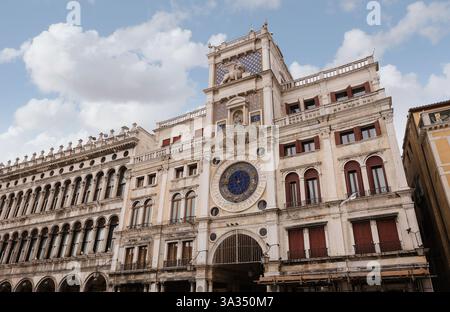Der historische Uhrenturm in Venedig, Italien, zeigt komplexe architektonische Details mit seiner kunstvollen Fassade und dem großen Uhrenfenster vor der Kulisse Stockfoto