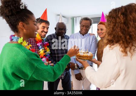 Eine lebhafte Gruppe von Menschen feiert einen Geburtstag mit bunten Partyhüten und einem Kuchen. Sie teilen ein Lächeln und schaffen eine warme und festliche Atmosphäre voll von Stockfoto