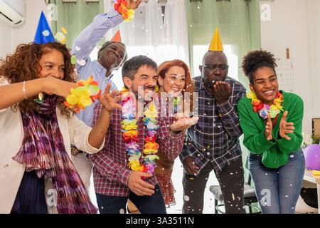 Eine bunte Gruppe von Freunden feiert fröhlich einen Geburtstag und wirft buntes Konfetti in die Luft, während sie festliche Partyhüte und Blumenhalsketten tragen Stockfoto