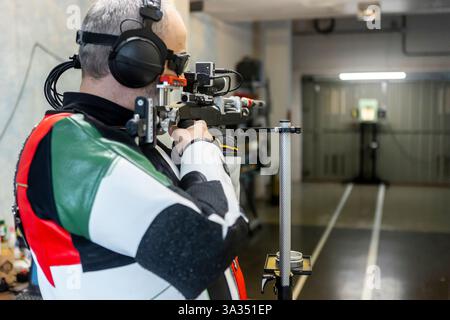 Ein blinder paralympischer Shooter übt in einer Halle und verfeinert seine Fähigkeiten mit Präzisionsausrüstung und Kopfhörern. Sportliche Ausdauer und Anpassungsfähigkeit Stockfoto