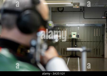 Blinde Athlet konzentriert sich auf ein Ziel bei einem olympischen Schießereignis. Das Bild erfasst die Intensität und Konzentration, die bei adaptiven Sportarten erforderlich sind. Kopfsatz Stockfoto