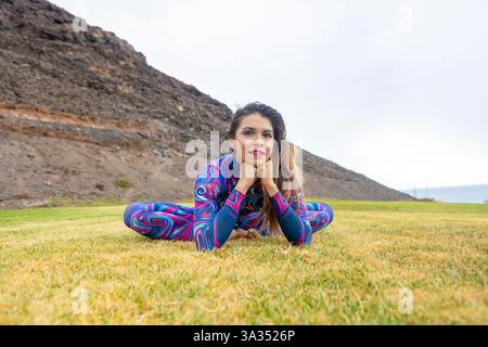 Eine Frau in einem lebendigen, gemusterten Kostüm posiert anmutig auf dem Gras und symbolisiert Freiheit und LGBTQIA+ Stolz. Der natürliche Hintergrund verleiht ihr mehr Selbstvertrauen Stockfoto
