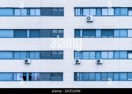 Eine moderne Stadtfassade mit einem weißen Wohngebäude mit Fenstern und externen Klimaanlagen. Stockfoto