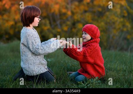 Ein Mädchen und ein Junge, Geschwister, genießen einen verspielten Moment im Freien an einem Herbsttag und halten die Hände warm in einem Park umgeben von farbenfrohen Blättern. Stockfoto
