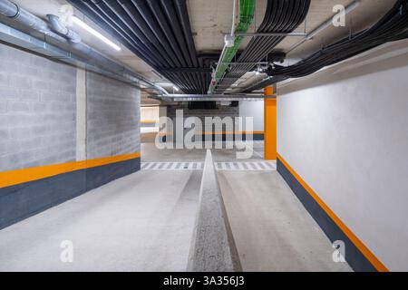 Dieses Bild zeigt eine gut beleuchtete, moderne Tiefgarage mit leuchtenden orangefarbenen und weißen Sicherheitsmarkierungen, effizienter Beleuchtung und strukturiertem P Stockfoto