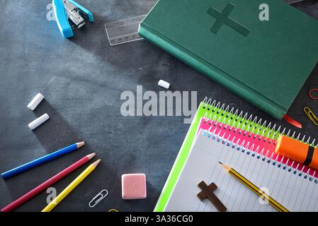 Religiöser pädagogischer Hintergrund mit Schulmaterial auf einer Tafel, wie Notizbücher, Buntstifte, ein Lineal und Radiergummi und eine grüne Bibel. Obere V Stockfoto