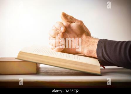 Person betet mit Händen, die über ein religiöses Buch gekreuzt wurden, auf einem Holztisch und weißem isolierten Hintergrund. Seitenansicht. Stockfoto