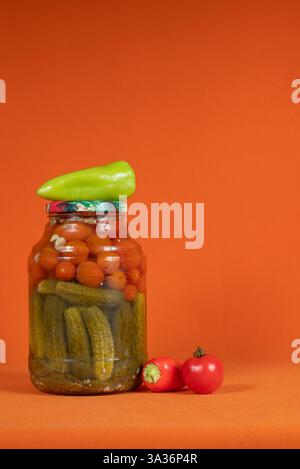 Hausgemachte eingelegte Dosentomaten und Gurken in einem Glas auf einem leuchtend orangen Hintergrund Stockfoto