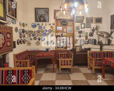 Ein gemütliches, traditionelles Zimmer mit gemusterten Kissen, dekorativen Tellern an der Wand und verschiedenen gerahmten Kunstwerken. Das Zimmer hat eine warme, einladende Atmosphäre Stockfoto