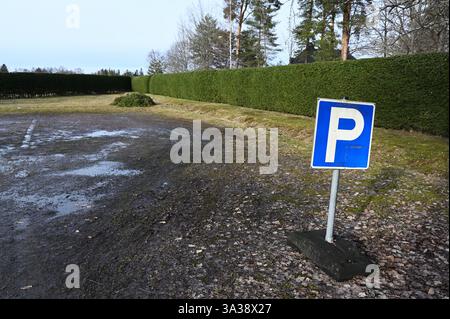 Ein blau-weißes Parkschild steht leicht geneigt auf einem Außenparkplatz mit einer matschigen, nassen Oberfläche, die mit herabfallenden Blättern bedeckt ist. Das Los erscheint un Stockfoto