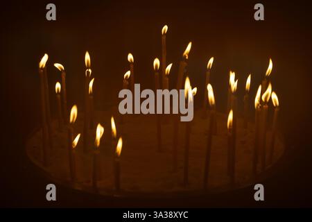 Kleine Kerzen in Sand, deren Flammen warm vor dunklem Hintergrund leuchten, die Gefühle von Spiritualität, Gelassenheit und Reflexion wecken. Stockfoto