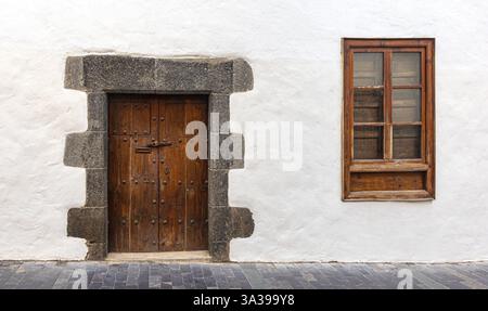 Alte braune Holztür und Fenster sind in eine weiße Wand mit Steinrahmen und Pflaster eingefasst Stockfoto
