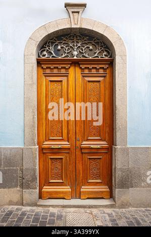 Die verzierte Doppeltür aus Holz mit aufwändigen Schnitzereien, einem dekorativen Heckspiegel aus Eisen und einem bogenförmigen Steinrahmen verleiht einem Bügel einen Hauch von Eleganz Stockfoto