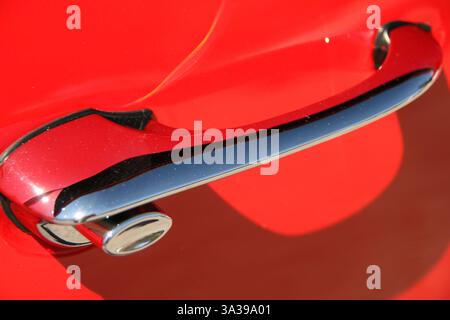 Ein klassischer, altmodischer Türgriff aus Chrom bei einem klassischen roten Auto. Stockfoto