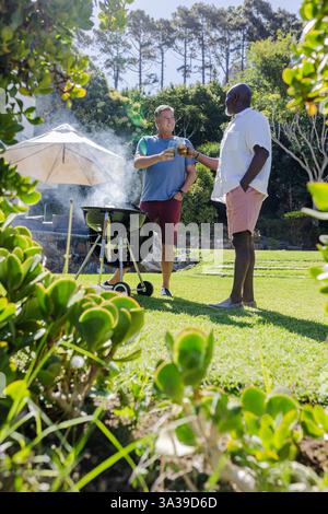 Ältere Freunde genießen Barbecue und Getränke im sonnigen Hinterhof und feiern die Zweisamkeit Stockfoto