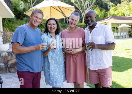 Lächelnde Seniorenfreunde genießen gemeinsam Drinks im sonnigen Hinterhof Stockfoto