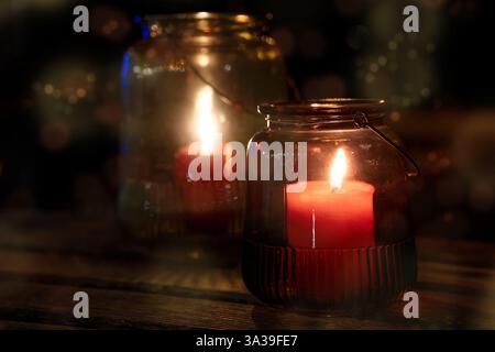 Hausgemachte Laternen, rote Kerzen in Glasgläsern auf einem Tisch in einer dunklen Sommernacht, Garten- oder Partydekoration, Kopierraum, ausgewählter Fokus Stockfoto