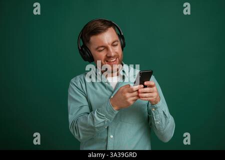 Schwarzes Smartphone in den Händen. Der Mann steht vor dem Hintergrund im Studio. Stockfoto
