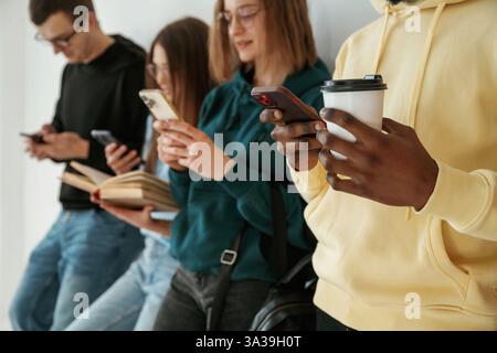 Mit Smartphones beschäftigt. Eine Gruppe junger Menschen steht vor weißem Hintergrund. Stockfoto