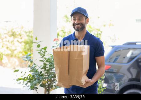 Glücklicher Kuriermann in blauer Uniform mit zwei Papiertüten. Stockfoto