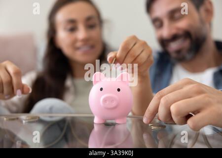 Nahaufnahme der Hände, die Bargeld in die rosa Schweinebank werfen Stockfoto