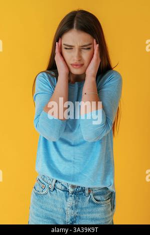 Starke Kopfschmerzen. Die junge Frau ist auf gelbem Hintergrund. Stockfoto