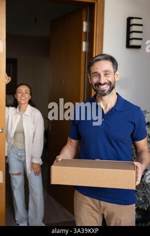 Glücklicher lateinamerikanischer Liefermann mittleren Alters, der ein Paket zu den Kunden transportiert Stockfoto