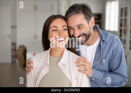 Glückliches, attraktives Paar, das eng beieinander steht, umarmt und wegblickt Stockfoto