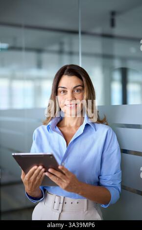Lächelnde, reife Geschäftsführerin, die im Büro ein Tablet hält. Hochformat. Stockfoto