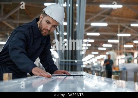 Prüfung der Materialqualität, Kontrolle. Fabrikarbeiter ist mit Schutzhelm drinnen. Stockfoto